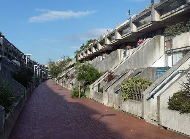 阶梯状混凝土住宅楼沿红砖步道两侧排列，各户露台种满绿植，是典型的粗野主义风格住宅区实景。