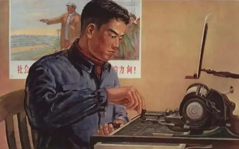 一位穿蓝色工装的男性打字员俯身用手指按压中文打字机的字模,身后墙上贴着一张工农题材宣传画,画中一人向前方伸手指引,配红色标语(内容被遮挡不可辨)。