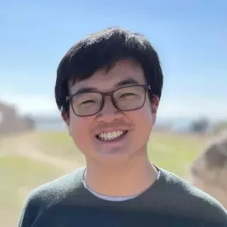 罗宇乐的肖像照,他戴眼镜面带微笑,背景为户外晴朗天空与草地。