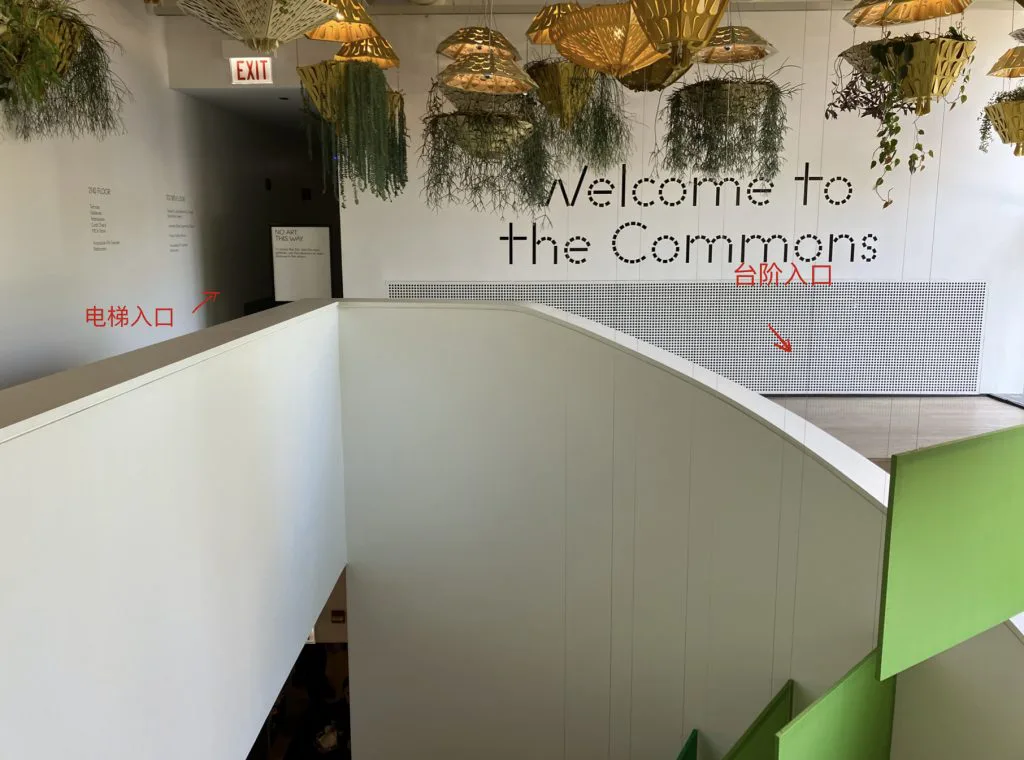 二楼大厅入口，头顶悬挂金色纸灯笼装饰，墙上写着'Welcome to the Commons'；红色箭头分别标注'电梯入口'（指向左侧狭窄转角）和'台阶入口'（指向右侧开阔的圆点花纹墙面）。